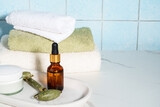 Fototapeta  - Skin care products in the bathroom. Face cream, serum bottle, jade roller and stack of towels.