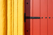 Detail of a traditional red wooden door with black metal hinge on a yellow wall