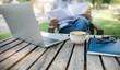 Asian man working outdoor on old wooden table with coffee drink checking business documents and using laptop working online