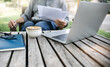 Asian man working outdoor on old wooden table with coffee drink checking business documents and using laptop working online