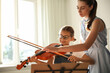 © New Africa - Young woman teaching little girl to play violin indoors