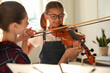 © New Africa - Young woman teaching little girl to play violin indoors