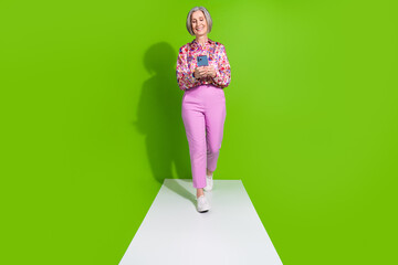 Sticker - Full length photo of sweet lady pink shirt walking promenade chatting modern device empty space isolated green color background