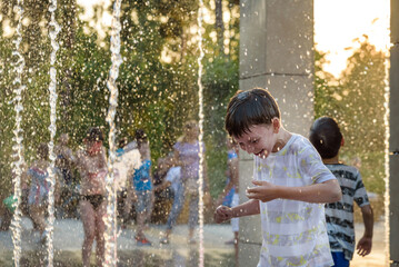 Wall Mural - Boys jumping in water fountains. Children playing with a city fo