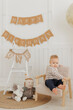 Portrait Happy caucasian little boy sits against background of holiday decorations and flags with inscription. Baby first birthday concept