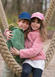  girl tenderly hugs her brother. Children sit on a swing in a city park and laugh. Brother and sister, children, family, friendship