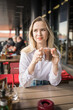 Gen z blonde woman drinks hot chocolate in summer cafe. Tasty beverage and break concept. Generation z people