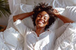 © sashka1313 - Cheerful African Woman Lying in Bed and Stretching Her Arms – Morning Routine and Wellness Concept. joyful African woman enjoying her morning routine, lying in bed and stretching her arms.