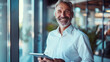 © Muhammad - Older smiling business man holding tablet standing in office. Middle aged happy businessman manager investor using tab computer, mature male executive looking at camera at work. Portrait