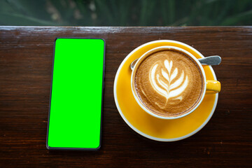 Hot coffee latte with latte art milk foam in cup mug,smartphone with empty screen on wood desk on top view. As breakfast In a coffee shop at the cafe,during business work concept,vintage style