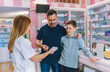 Cheerful pharmacist chemist woman giving vitamins, medicine to father and son.