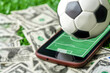 Soccer ball on smartphone and money on green grass background, sports gambling via smartphone apps