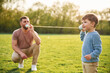 © standret - Talking by using paper cup telephone. Happy father with son are having fun on the field at summertime