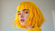 A woman with yellow hair and makeup. Concept of confidence and boldness, as the woman's bright hair and makeup draw attention to her face. Shaggy lob haircut with fringe in a gray Background