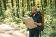 Old fashioned paper map in hands. Bearded man is in the forest at daytime