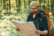 Focused on reading the map. Bearded man is in the forest at daytime