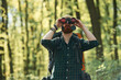 Discovering new place with binoculars. Bearded man is in the forest at daytime