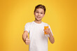 Strengthen immunity. Cool teenager with orange juice gesturing thumb up, studio background