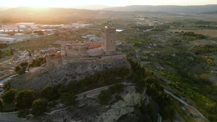 Wall Mural - Drone circling around the Castle of Biar. Castel is situated on top of the hill, surrounded by the medieval village. Beautiful warm colours at sunset. Travel destination in Alicante province, Spain.