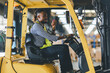 Man worker at forklift driver happy working in industry factory logistic ship. Man forklift driver in warehouse area. Forklift driver sitting in vehicle in warehouse.