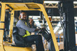 © kanpisut - Man worker at forklift driver happy working in industry factory logistic ship. Man forklift driver in warehouse area. Forklift driver sitting in vehicle in warehouse.