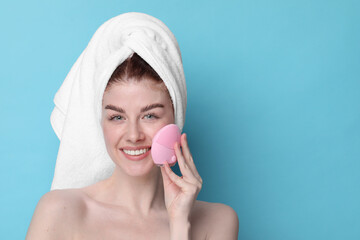 Canvas Print - Washing face. Young woman with cleansing brush on light blue background, space for text