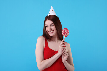 Poster - Happy woman in party hat with lollipop on light blue background