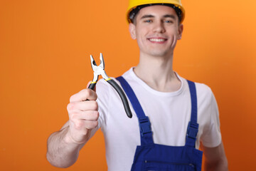 Sticker - Young man holding pliers on orange background, selective focus