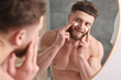 © New Africa - Handsome man applying moisturizing cream onto his face near mirror in bathroom