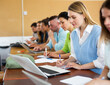 © JackF - Woman sitting in classroom during lecture in university and using laptop. Students sitting in a row.