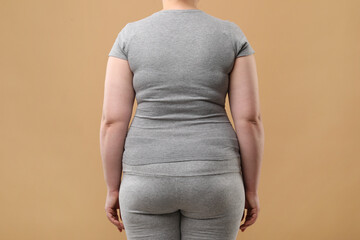 Wall Mural - Overweight woman in grey clothes on beige background, back view