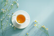 Cup of herbal tea surrounded by camomiles on a light blue background with copy space..