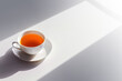 White cup of tea with a sharp shadow on a bright white surface with copy space