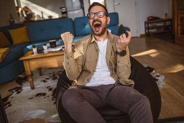 Wall Mural - Adult man with eyeglasses play video games on his phone at home