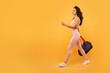 © Prostock-studio - A young woman with long hair, dressed in a form-fitting activewear outfit, walks with purpose while carrying a gym bag, isolated on yellow background