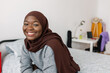 Portrait of happy young proud woman in muslim headscarf relaxing at home sitting on bed