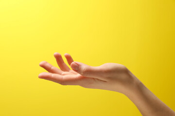 Wall Mural - Woman holding something in hand on yellow background, closeup