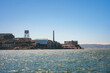 View of Alcatraz Island on a clear day in San Francisco Bay. Features water tower, buildings, smokestack, and boat, capturing former prison's history.