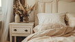Close up of bedside cabinet near bed with beige bedding, French country interior design of modern bedroom, Bedside table with lamp and books in cozy bedroom, Beige bedding with pillows on comfortable 