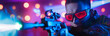 Focused player in vivid neon lights aims with a laser gun in an intense laser tag game, showcasing dynamic motion, precision, and immersive gaming experience in a colorful arena