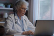 © Enigma - Professional senior female doctor is focused while consulting with patients online, using a laptop in her office with soft ambient lighting