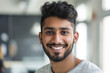 © Enigma - Close-up portrait of a cheerful young man with a stylish beard and a warm smile, posing indoors with a blurred background, exuding confidence and positivity
