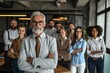 © Iigo - Portrait of confident senior businessman standing with his team in background at office