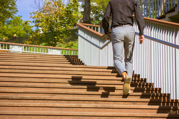 Business man in business style climbing confidently up wooden steps Success, extension forward concept. Men's shoes and legs on staircase Urban people