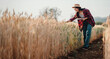 © Satori Studio - Diligent farmer bends over to examine the quality of the wheat in her field, taking notes to ensure a successful harvest season.