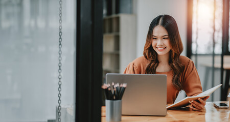 Wall Mural - Young woman is smiling as she works on her laptop in a warmly lit, cozy workspace with a pleasant ambiance.