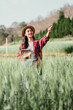 © Satori Studio - Smiling confidently, a female farmer uses a tablet while pointing to a spot in her thriving wheat field, integrating modern technology with traditional farming.
