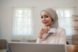 A young Muslim woman wearing a hijab sat contentedly shopping online and holding a credit card.