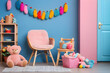 Warm composition of kid room interior with blue wall, kitchen for kids, stylish armchair, colorful garland, plush toys, wooden block toys, pink basket and personal accessories. Home decor. Template.