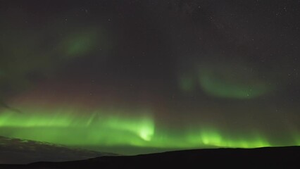 Wall Mural - The dark still waters of the fjord are illuminated by the beautiful dance of the Aurora Borealis in the winter sky.